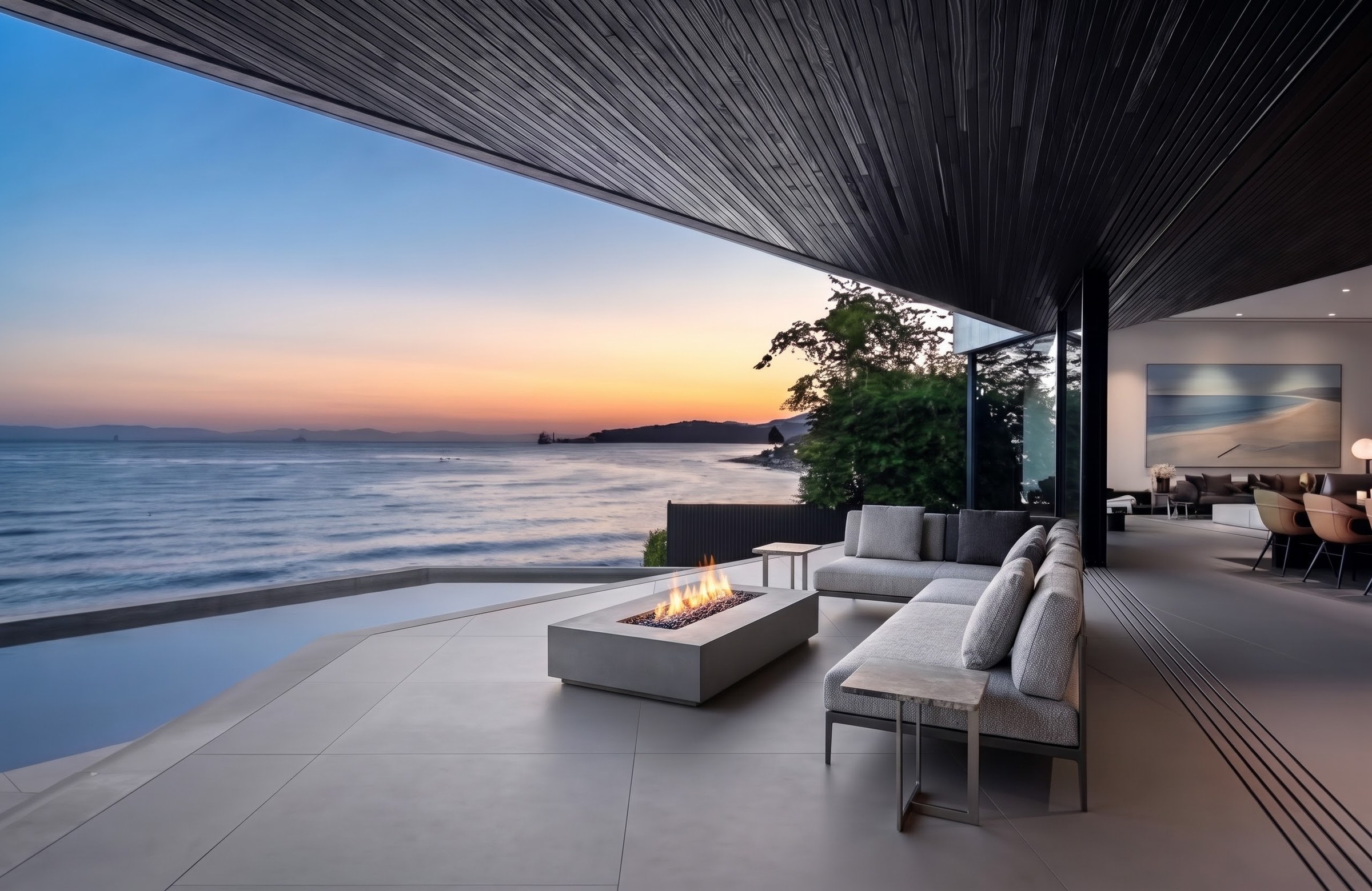 Oceanfront patio with infinity pool, fire table and lounge seating at sunset at a West Vancouver home